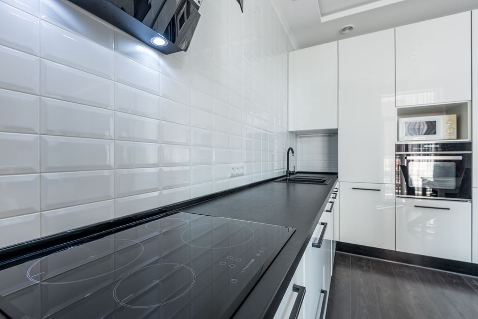 Interior of modern light white kitchen furnished with white cupboards and appliances with wooden floor and tiled wall