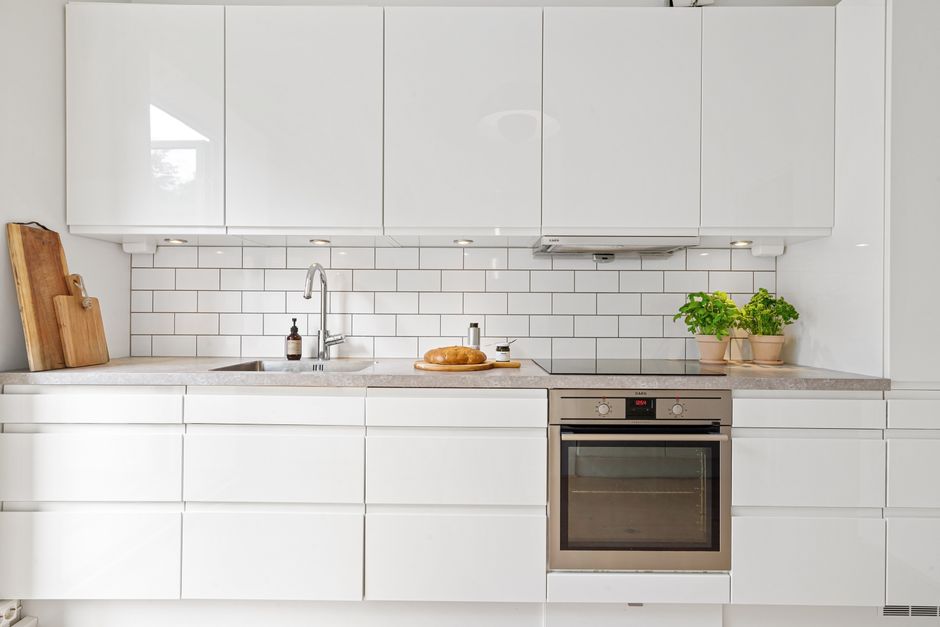 Sleek white kitchen featuring subway tiles, built-in oven, herbs, and bread for a modern touch.