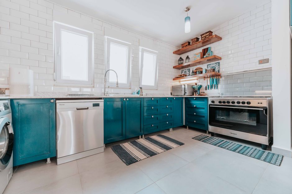 Bright modern kitchen with blue cabinets, stainless steel appliances, and open shelving.